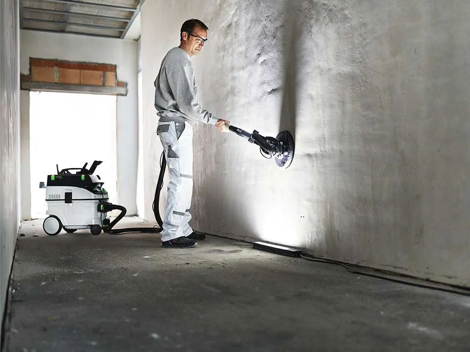 Egy mesterember megvilágítja a falat a festő Kontroll lámpa segítségével és lecsiszolja azt